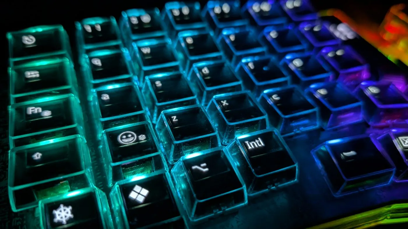 Close-up of transparent keycaps lit in a green-to-purple gradient, each one showing its own OLED legend — letters, an emoji face, a Windows logo and an "Intl" key